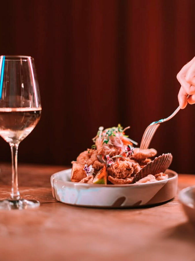 Entrante de marisco del restaurante Tatel Ibiza con copa de vino blanco sobre la mesa.