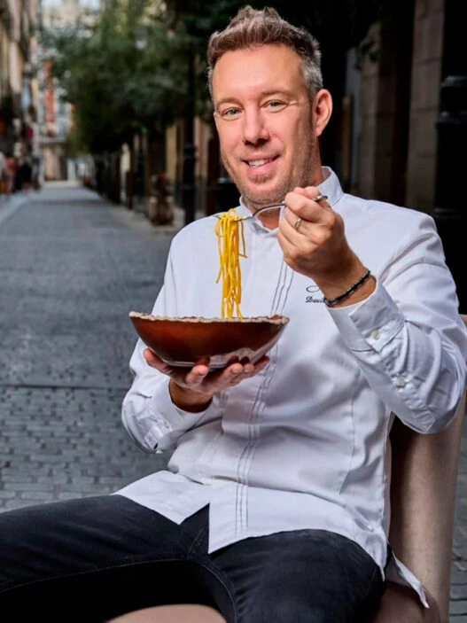 El chef italiano Davide Bonato comiéndose un plato de pasta en mitad de una calle del barrio de Malasaña de Madrid.