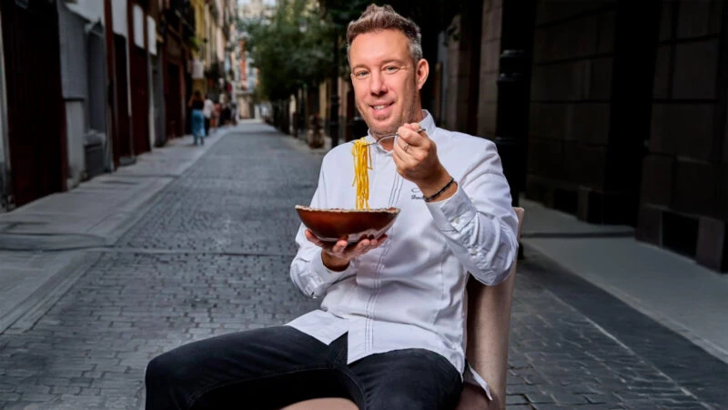 El chef italiano Davide Bonato comiéndose un plato de pasta en mitad de una calle del barrio de Malasaña de Madrid.
