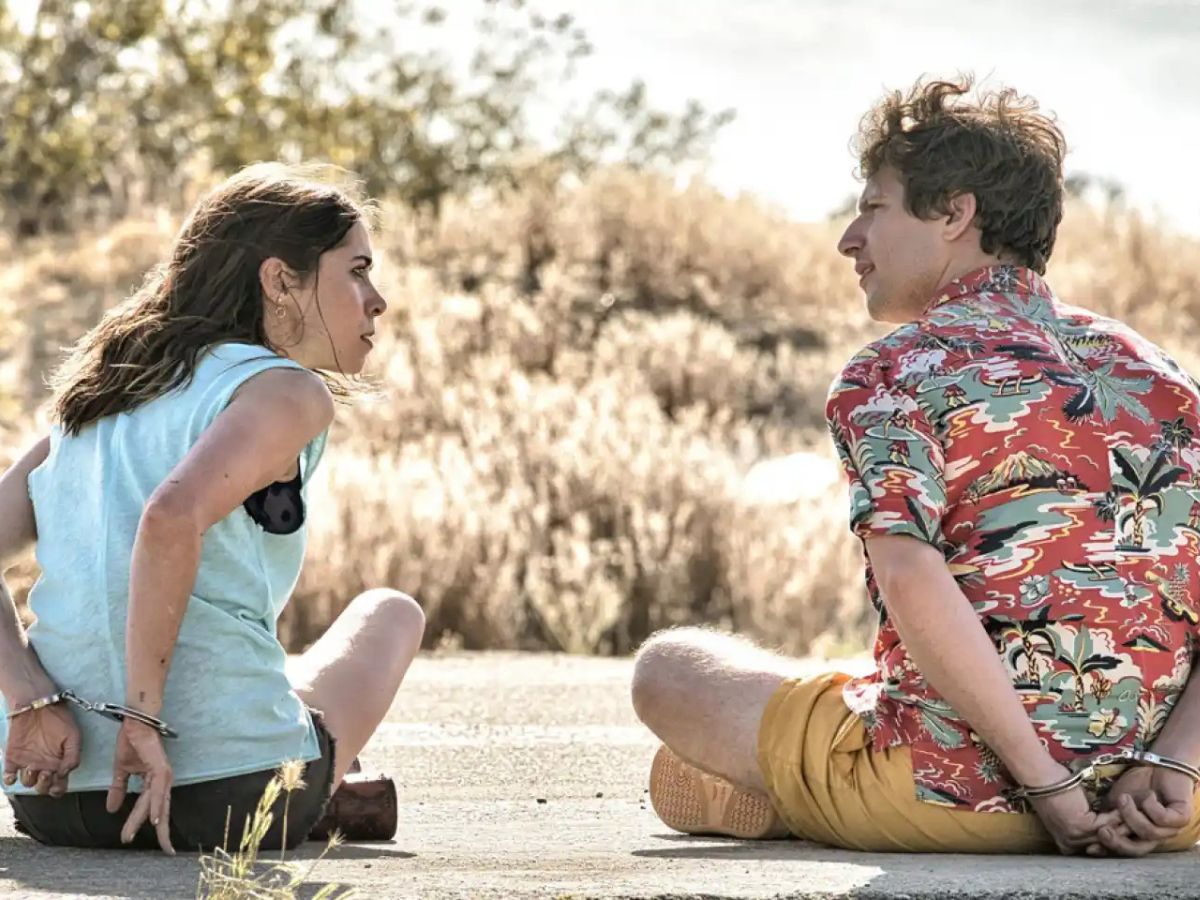 Escena de la película Palm Springs en la que se ve a sus protagonistas esposados y sentados en una carretera