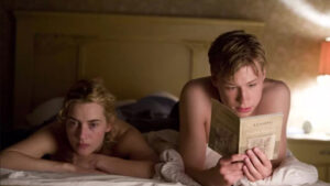 Una pareja en la que el chico le lee un libro a la chica, ambos están en la cama. Imagen para encabezar un artículo sobre los mejores libros imprescindibles que todos deberíamos leer al menos una vez en la vida.