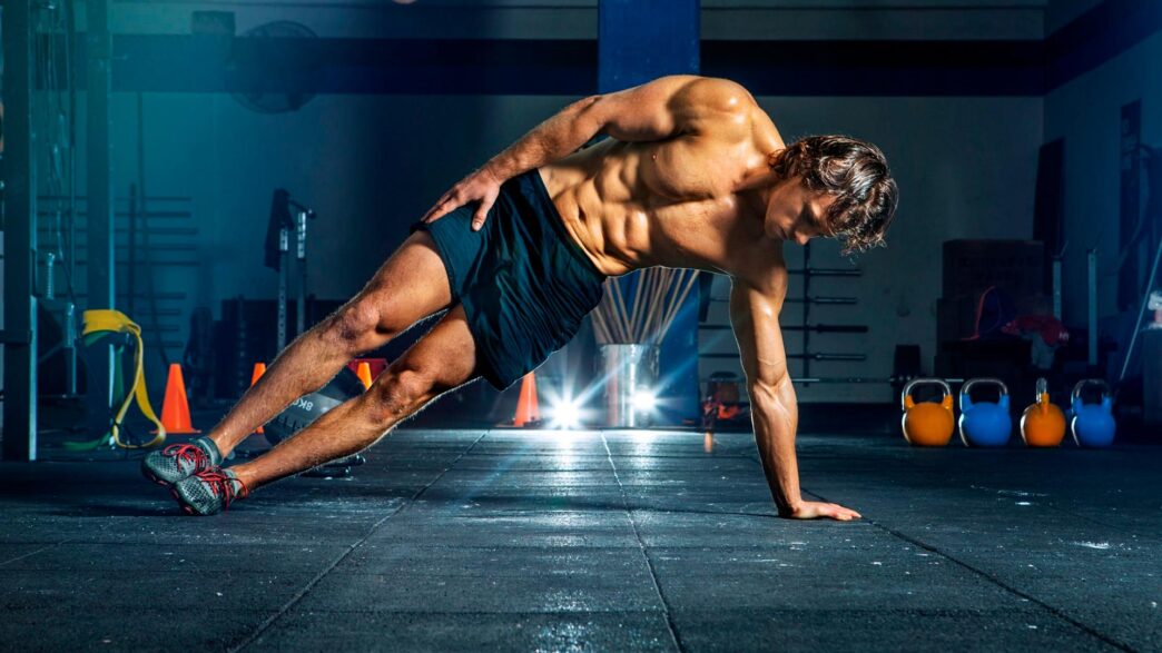 chico joven, de unos 20 años haciendo una plancha lateral en un gimnasio.
