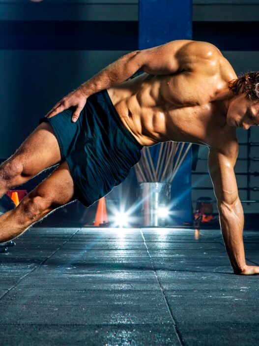 chico joven, de unos 20 años haciendo una plancha lateral en un gimnasio.