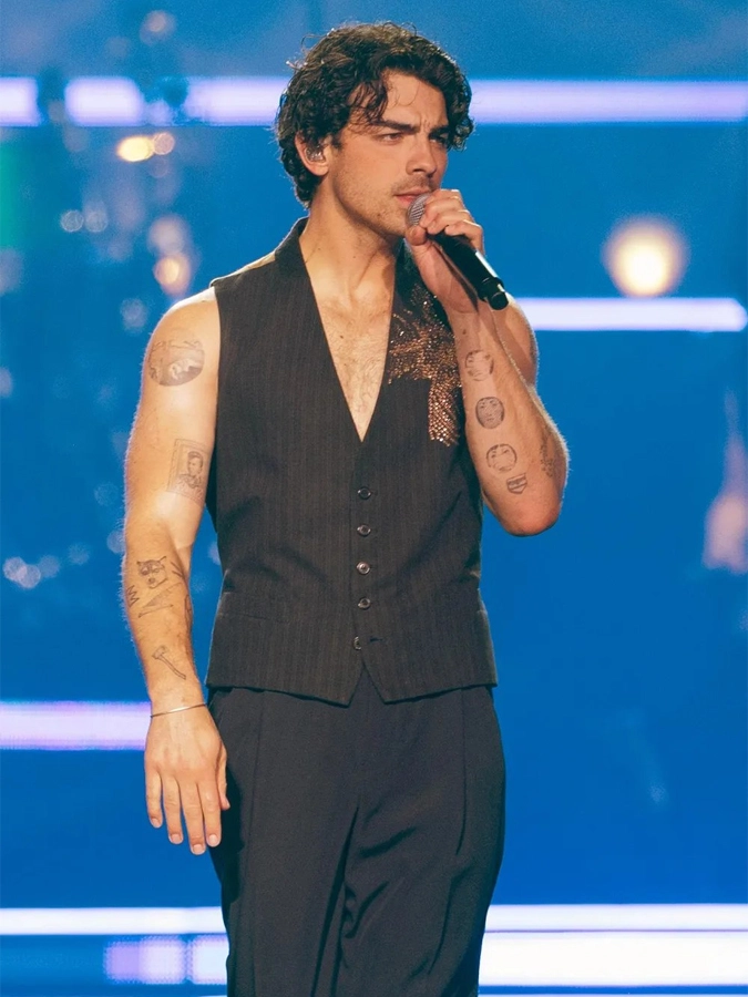 Joe Jonas, con los brazos con parches de tatuajes, cantando en un concierto