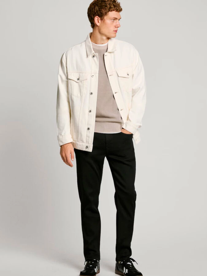 hombre vestido con un pantalón negro combinado con un jersey neutro y una chaqueta denim blanca