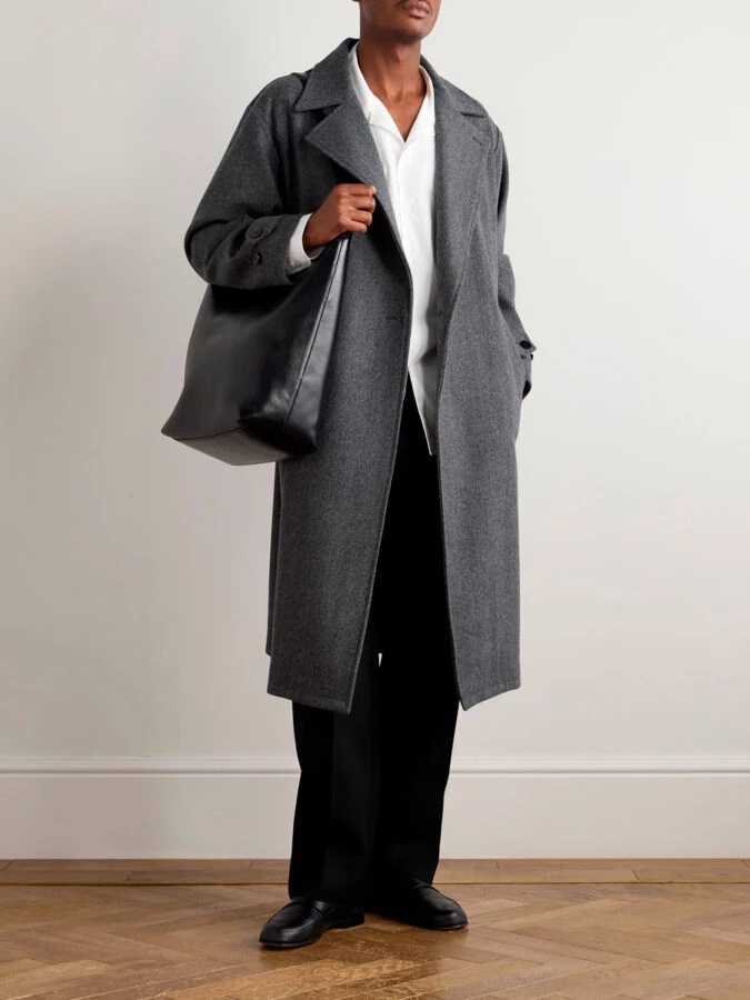 hombre vestido con un pantalón negro combinado con una camisa blanca y un abrigo largo gris