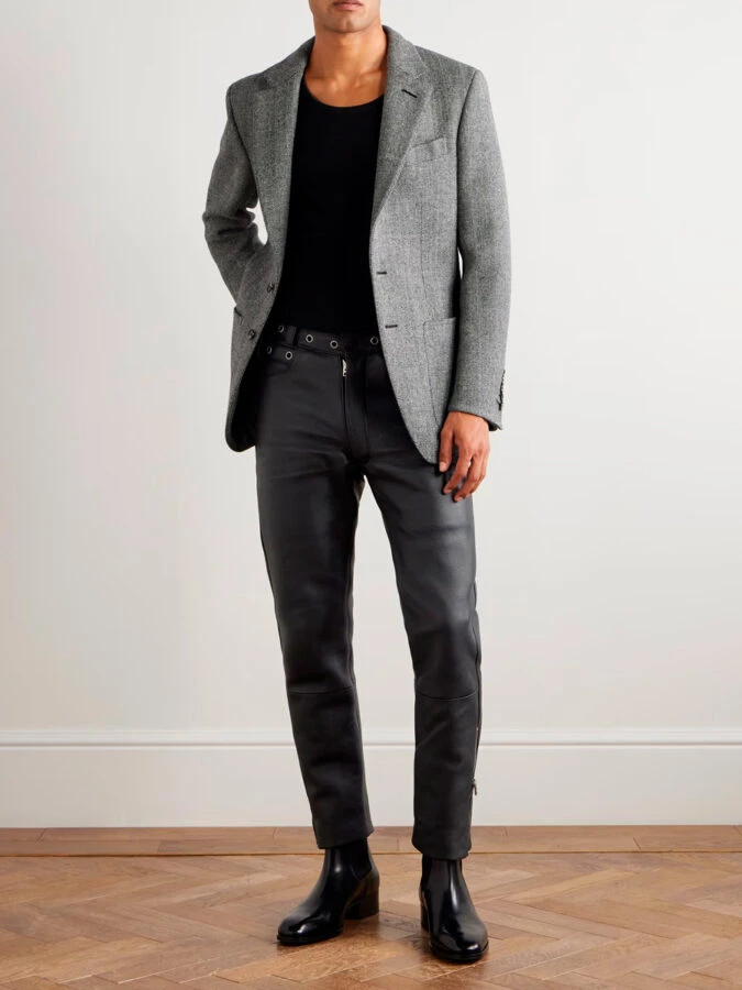 hombre vestido con un pantalón de cuero negro, una camiseta negra y una chaqueta gris