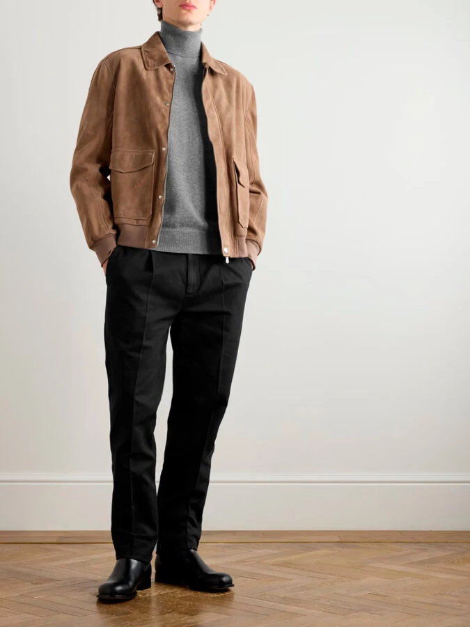 hombre vestido con un pantalón negro combinado con un jersey de cuello alto gris y una chaqueta marrón