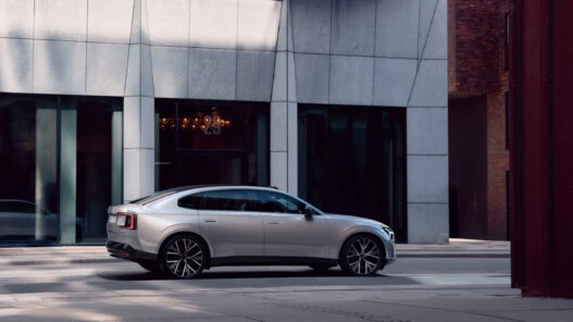 Volvo ES90 2025 en color plateado circulando por una calle urbana con edificios modernos