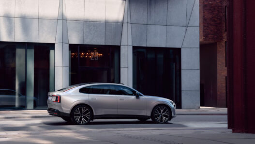 Volvo ES90 2025 en color plateado circulando por una calle urbana con edificios modernos
