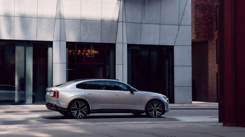Volvo ES90 2025 en color plateado circulando por una calle urbana con edificios modernos