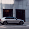 Volvo ES90 2025 en color plateado circulando por una calle urbana con edificios modernos