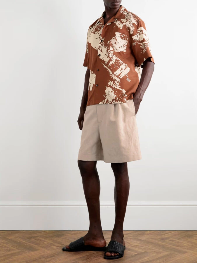 Look de verano con bermudas beige de lino, camisa marrón estampada y sandalias negras trenzadas de Bottega Veneta