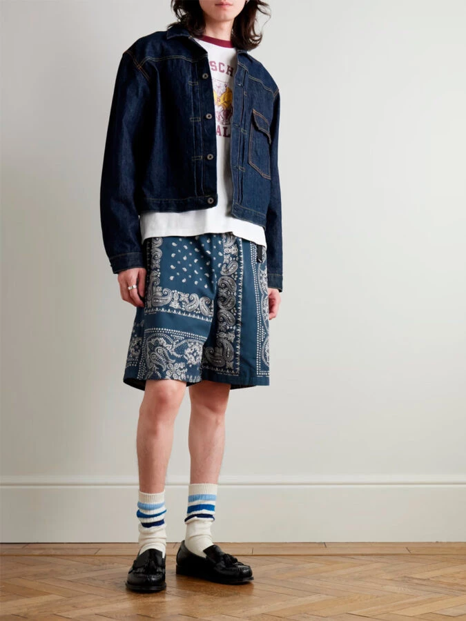 Estilo urbano con bermudas estampadas azul paisley, chaqueta vaquera, camiseta gráfica y mocasines negros con calcetines altos de Kapital