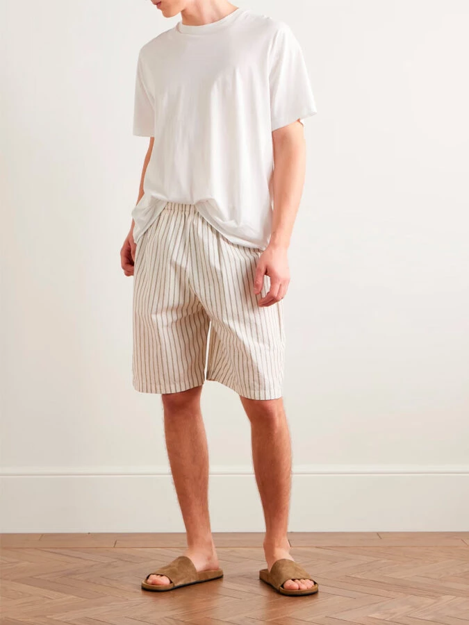 Look minimalista de verano con bermudas de rayas beige, camiseta blanca básica y sandalias de ante marrón de The Row