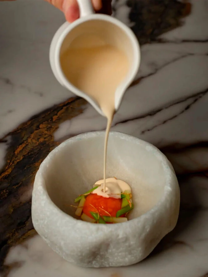 Emplatado en mesa de mármol con crema vertida sobre verdura y marisco en el restaurante Casona del Judío