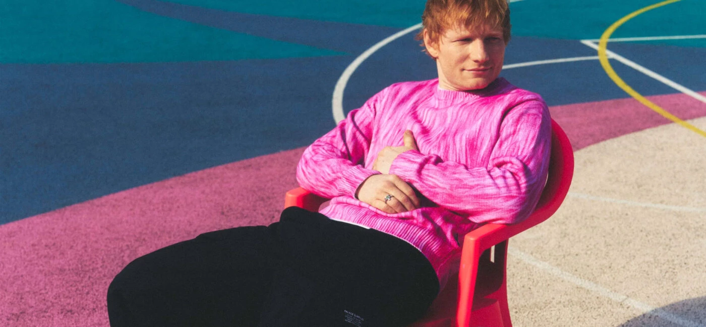 Ed Sheeran sentado en una silla roja con jersey rosa en una pista multicolor