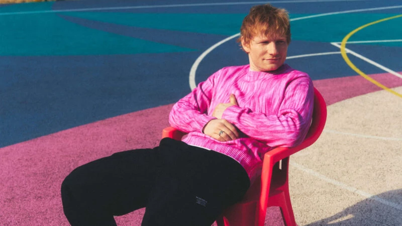 Ed Sheeran sentado en una silla roja con jersey rosa en una pista multicolor