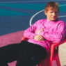 Ed Sheeran sentado en una silla roja con jersey rosa en una pista multicolor