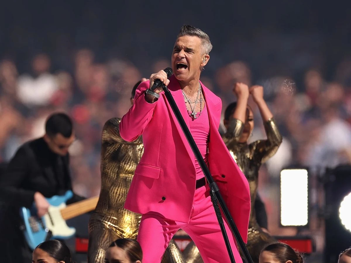 Robbie Williams cantando en directo con un traje rosa fucsia durante un concierto