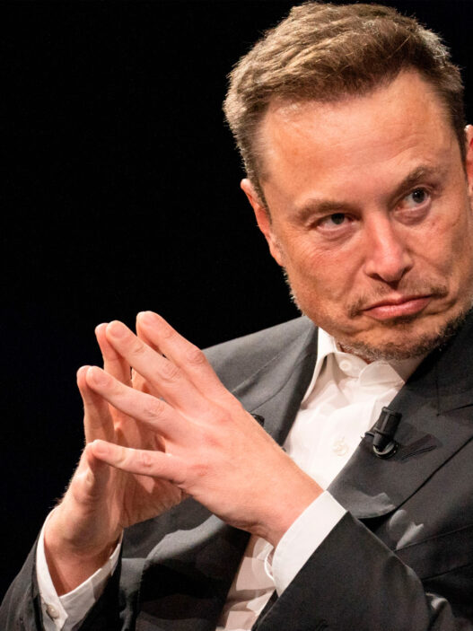 Elon Musk en un evento, con traje oscuro y manos entrelazadas