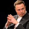 Elon Musk en un evento, con traje oscuro y manos entrelazadas