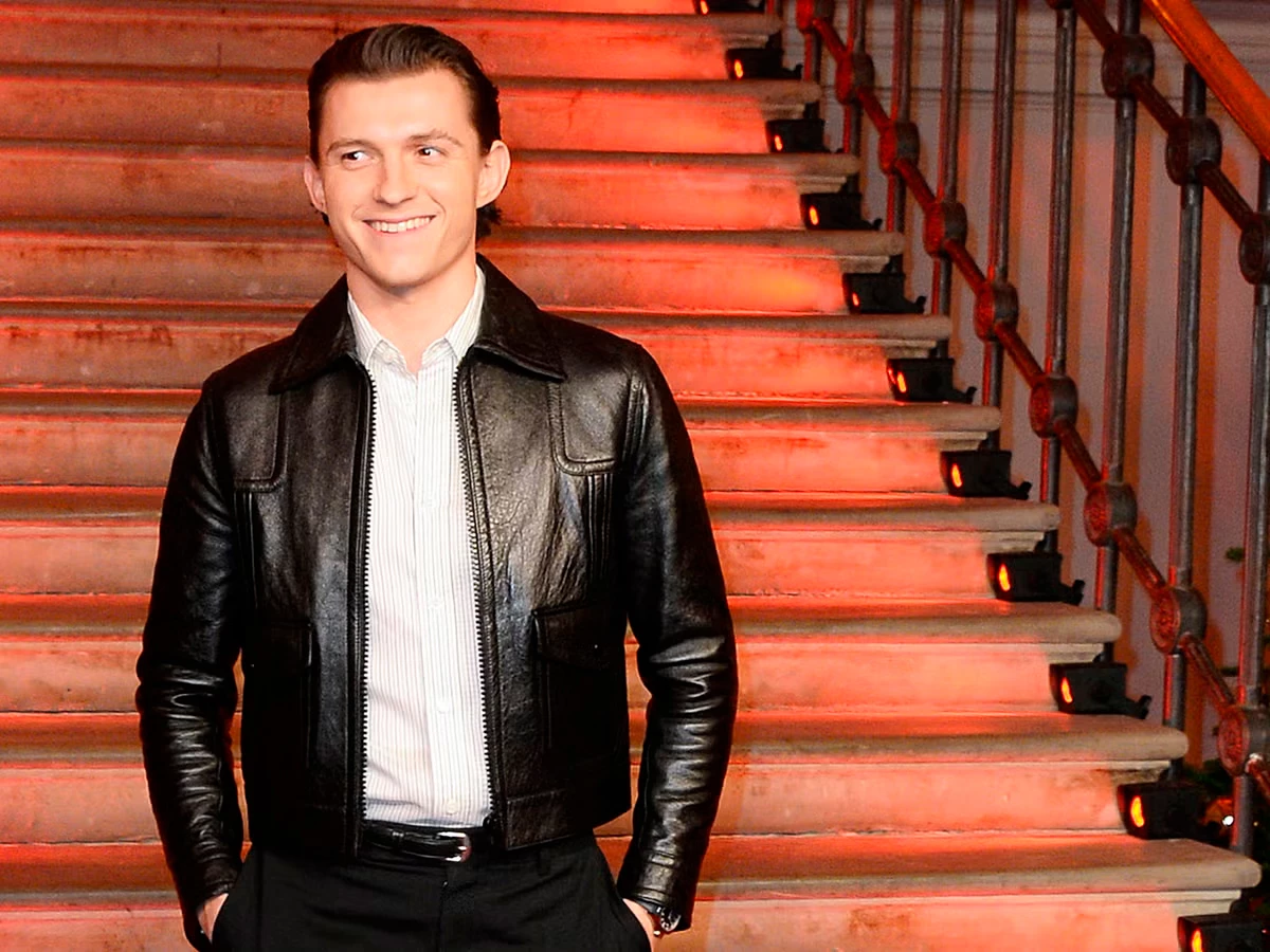 Tom Holland sonriendo en una alfombra roja con chaqueta de cuero