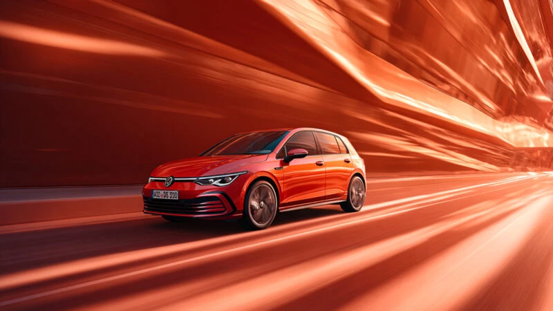coche Golf eHybrid 2025 de color rojo circulando en una ciudad de esilo futurista. Imagen para ilustrar un artículo sobre los coches que menos consumen de 2025