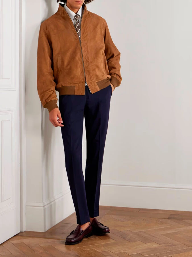 Chaqueta bomber de ante marrón con pantalón de traje azul marino, camisa blanca, corbata y mocasines burdeos sin calcetines