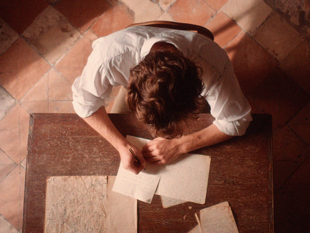 Hombre escribiendo una carta a mano en una mesa de madera imagen para ilustrar la conferencia "Las cartas de amor" de Luis Muiño en Aprendemos juntos BBVA