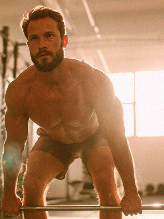 Hombre de 30 años atractivo levantando peso muerto en un gimnasio iluminado con luz natural