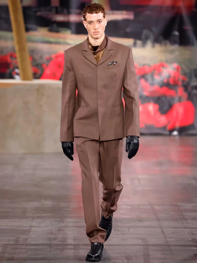 Modelo con traje marrón minimalista de cortes limpios con guantes negros de 032c otoño-invierno 2025.