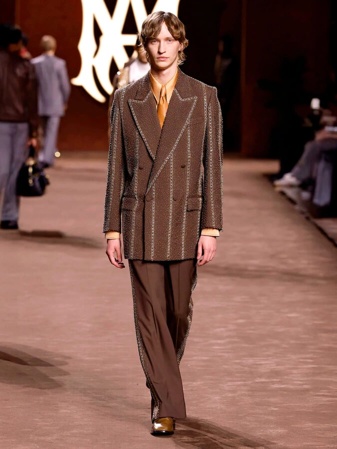 Modelo con traje marrón de rayas adornado con pedrería y camisa dorada de Amiri otoño-invierno 2025.