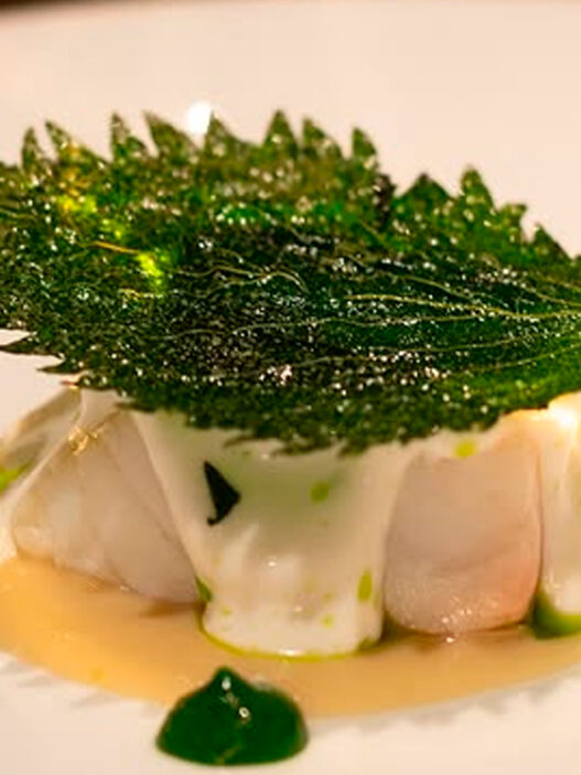Plato del menú Celebration del restaurante Caelis con lubina y hoja de shiso crujiente.