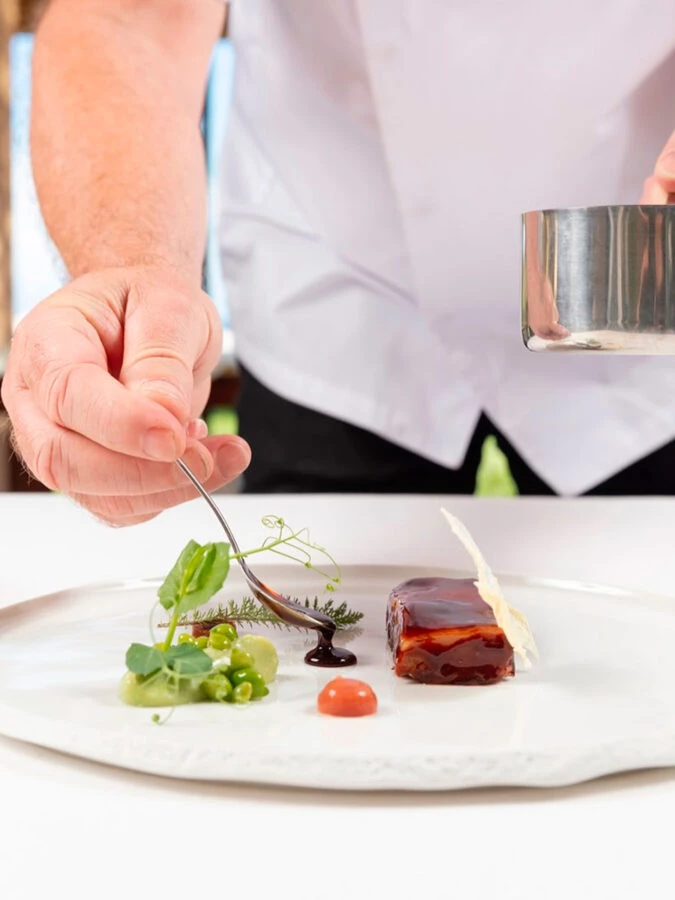 Emplatado del menú Aromas del Mediterráneo en Marc Fosh: el chef napando salsa junto a guisantes y brotes.