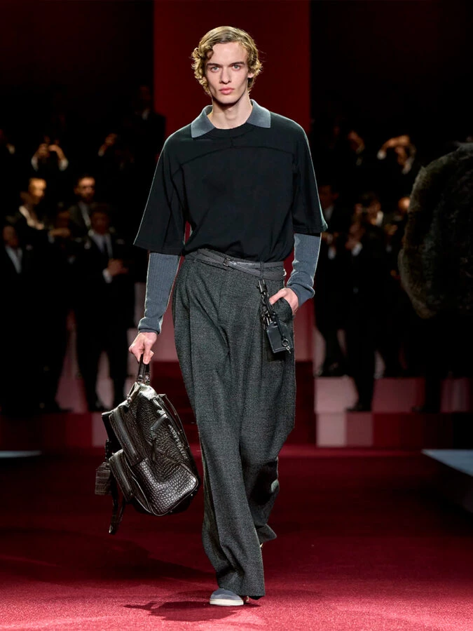 Modelo de Dolce & Gabbana con camiseta negra de manga corta sobre jersey gris y pantalón de pinzas