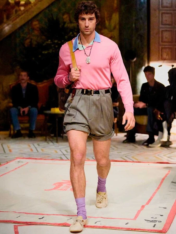 El actor Agustin della Corte desfilando para Versace vestido con un jersey rosa chicle, un polo azul y una bermudas holgadas