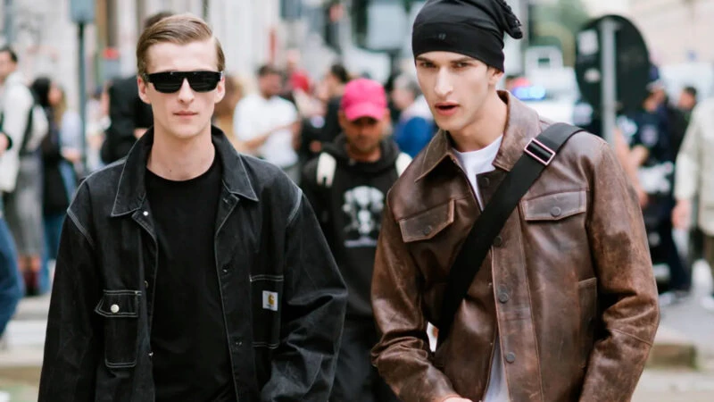dos chicos jóvenes, de veinte a treinta años, andando por la calle y vestidos con chaquetas actuales