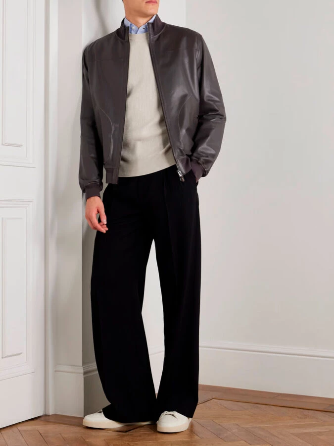 hombres vestidos con una chaqueta de cuero, jersey beige, camisa de cuadros clásica, pantalones negros fluídos y zapatillas blancas clásicas