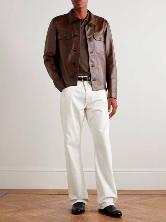 hombre vestido con una chaqueta de cuero marrón, un polo de punto color camel, unos pantalones denim blancos y botines negros