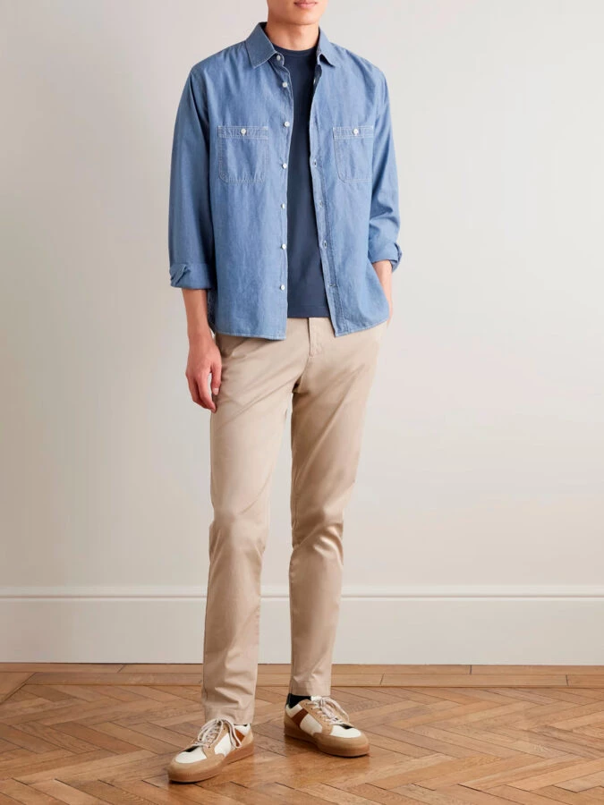 Hombre con pantalón beige, camiseta azul oscuro y sobrecamisa denim ligera combinados con zapatillas blancas