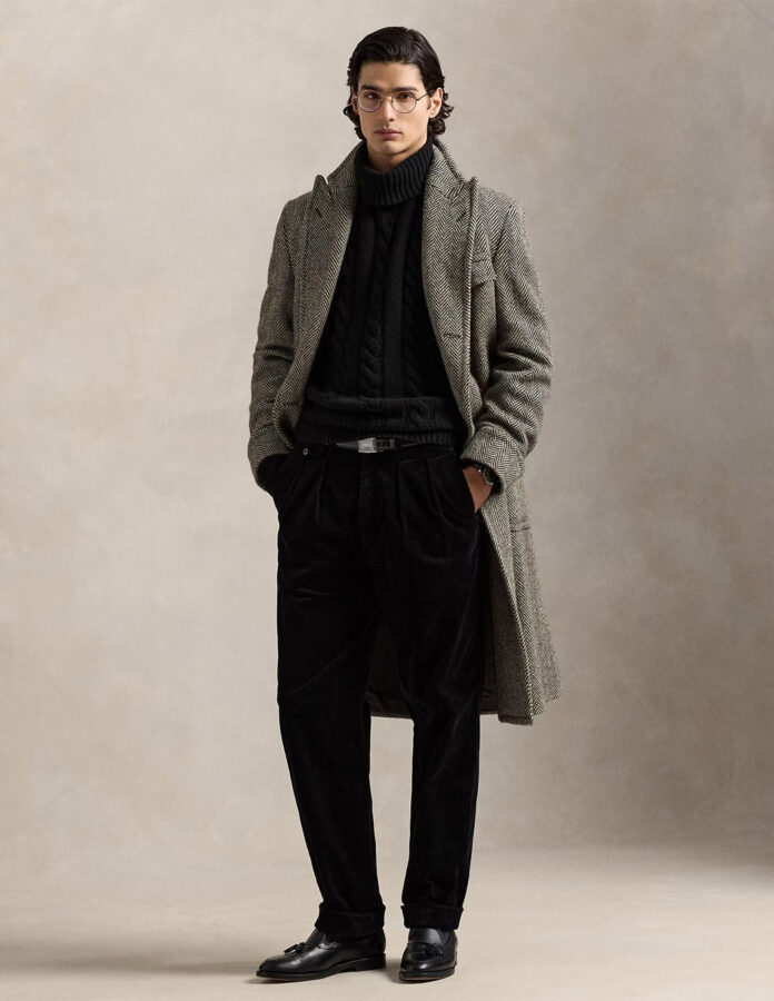 cómo combinar en pantalón negro de hombre: modelo vestido con un jersey de cuello alto negro y un abrigo largo de espiga gris.