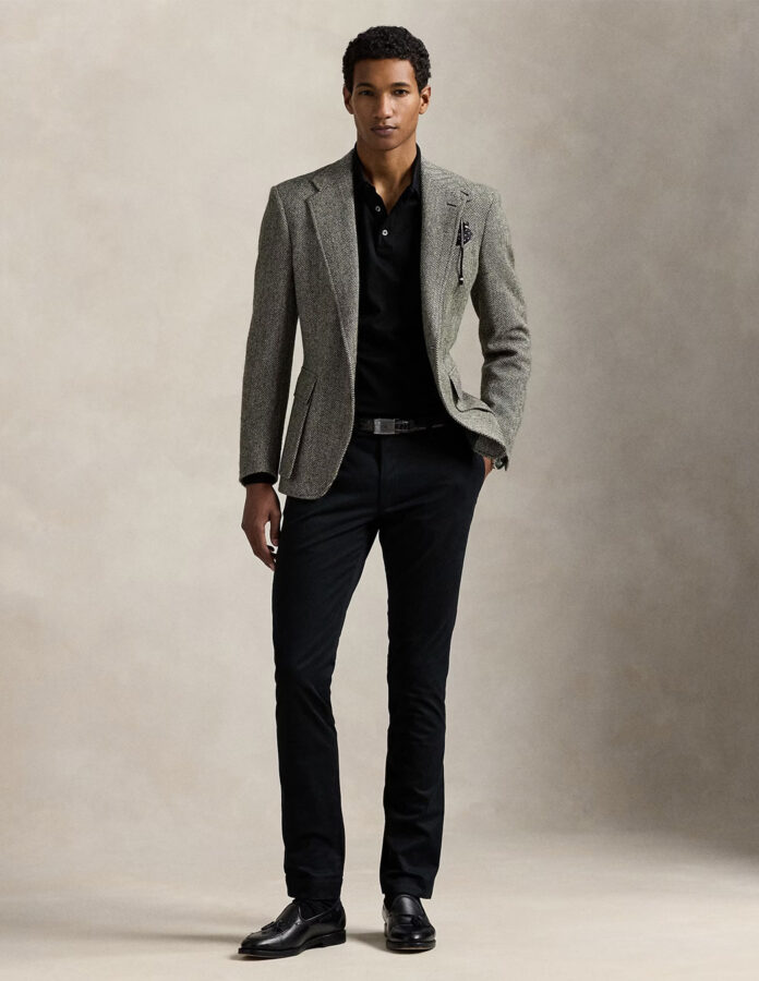 cómo combinar en pantalón negro de hombre: modelo masculino vestido con polo negro y chaqueta de espiga gris