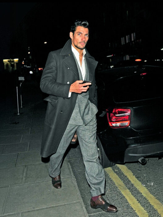 El modelo David Gandy caminando por la calle, de noche vestido muy elegante con traje y un abrigo largo
