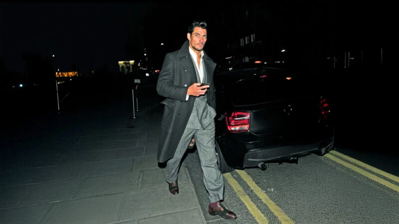 El modelo David Gandy caminando por la calle, de noche vestido muy elegante con traje y un abrigo largo