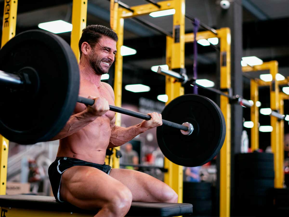 hombre sin camiseta entrenando biceps con barra en un gimnasio