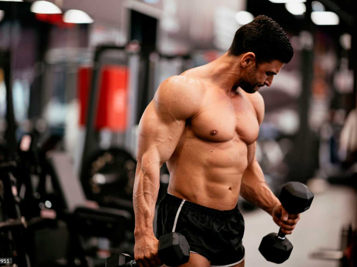 hombre en un gimnasio entrenando pull de biceps con mancuernas en un gimnasio y sin camiseta