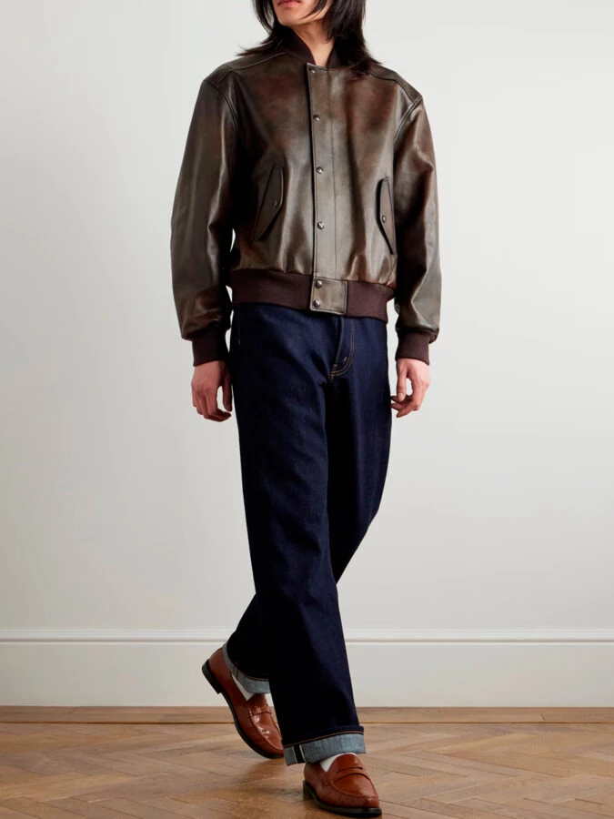 hombre vestido con una chaqueta de cuero tipo bomber, pantalones vaqueros rectos y mocasines marrones