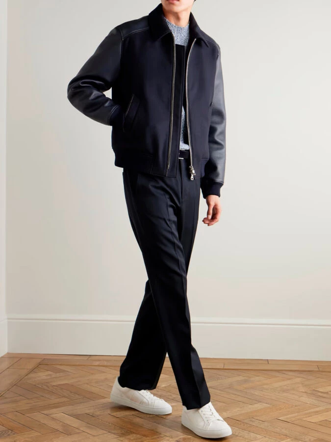 hombre vestido con una chaqueta tipo varsity combinada con un pantalón de traje y unas zapatillas blancas