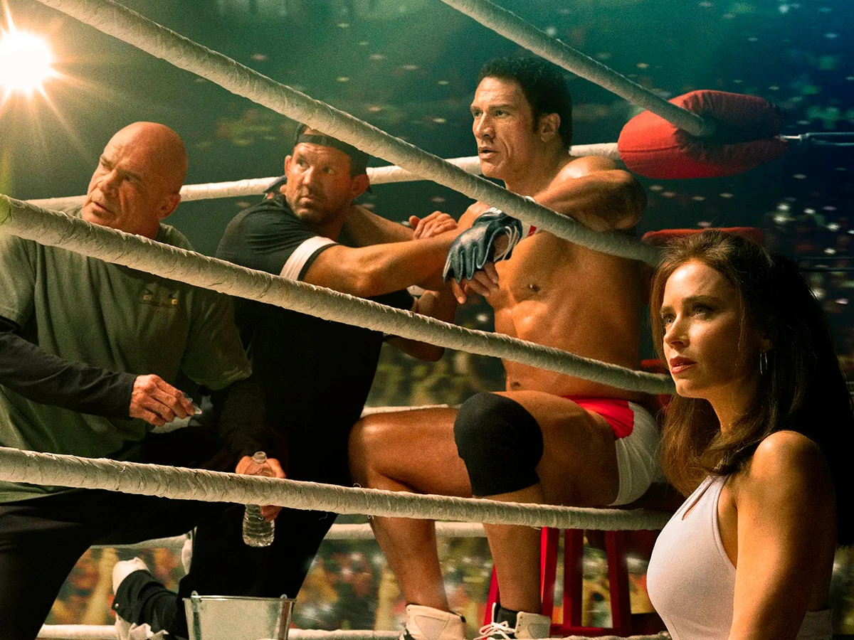 Escena de la película The Smashing Machine en la que se ve al actor Dwayne Johnson sentado en el ring de boxeo junto a otros actores